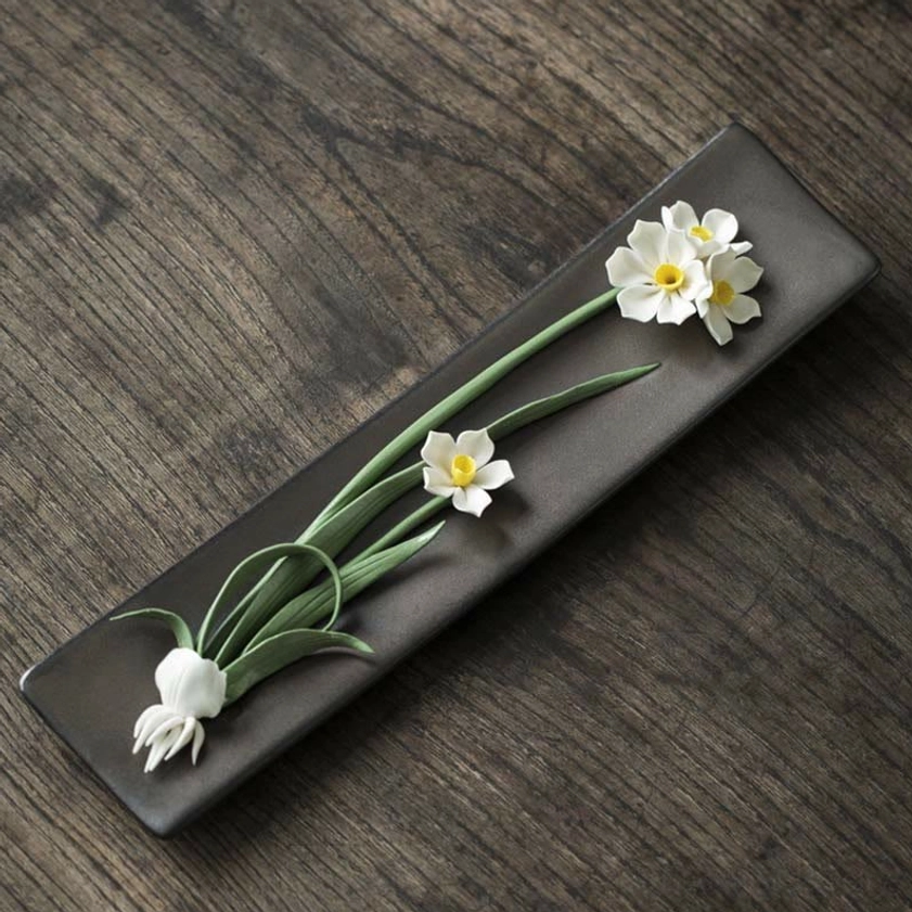 White daffodil ceramic incense burner with green stems, overhead close-up on dark wood table
