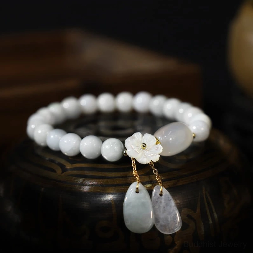 Polished white round jade beads with flower charm and jade drop pendants on dark wooden vessel