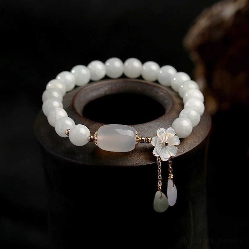 Close-up view of smooth white jade beads with flower charm and jade drop pendants on dark wood