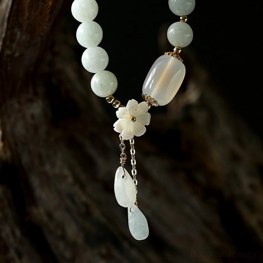 White jade beaded Buddhist bracelet with delicate shell flower charm and tiny teardrop pendants worn on wrist with red clothing