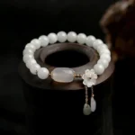 Natural white jade beaded bracelet with shell flower charm and teardrop pendants displayed on dark wooden stand close-up