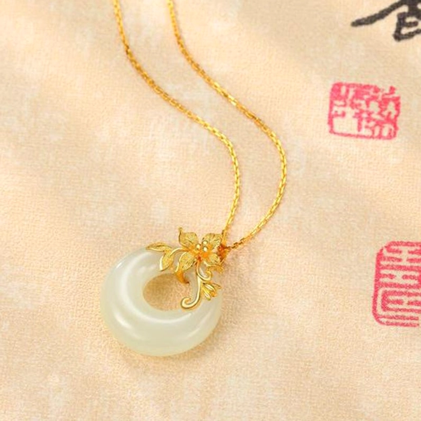 Overhead oblique view of white jade Buddhist necklace with delicate gold chain and floral copper hardware against antique calligraphy textile backdrop