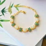 White jade and cyan jade lotus Buddhist bracelet with gold-toned chain, displayed overhead on a book with bamboo leaf decoration