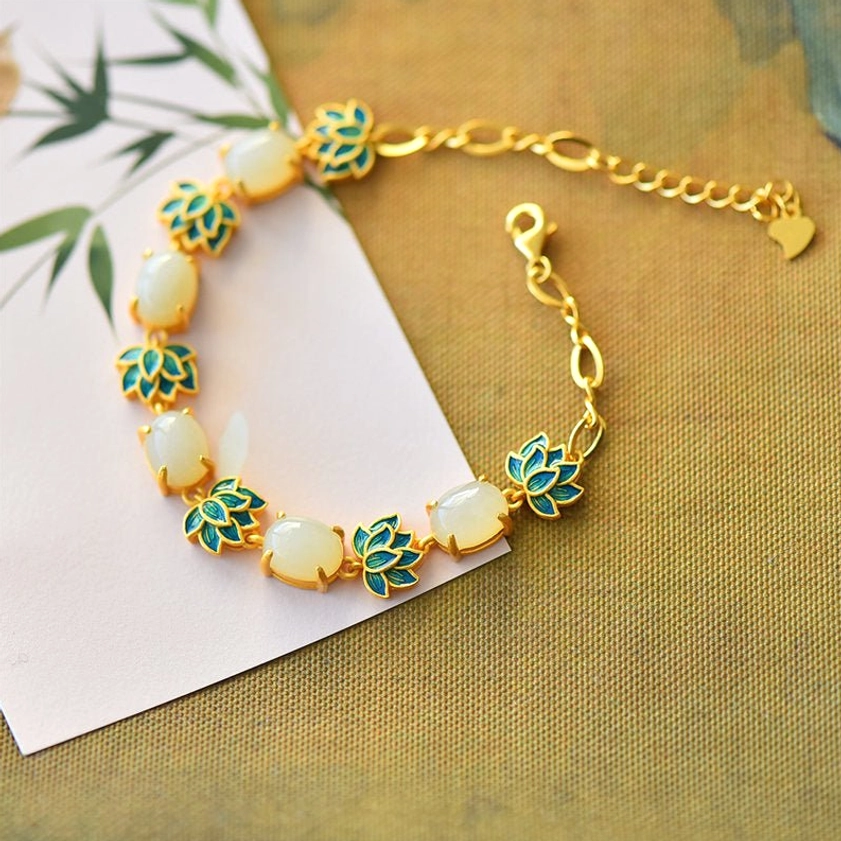 White jade lotus bracelet with heart-shaped clasp displayed on linen background with bamboo leaf decoration