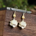 White jade lotus drop earrings displayed on wooden surface with dual-tone silver and gold metal details
