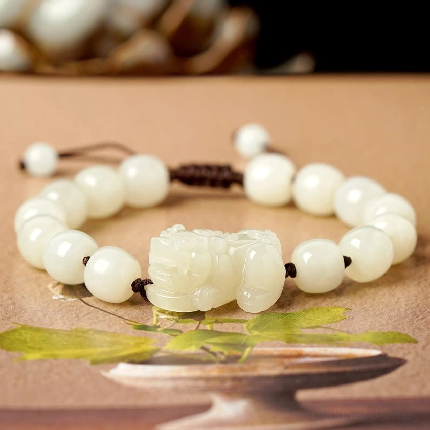 Barrel-shaped white jade beads with Pixiu charm and brown cord, high-angle shot with botanical styling