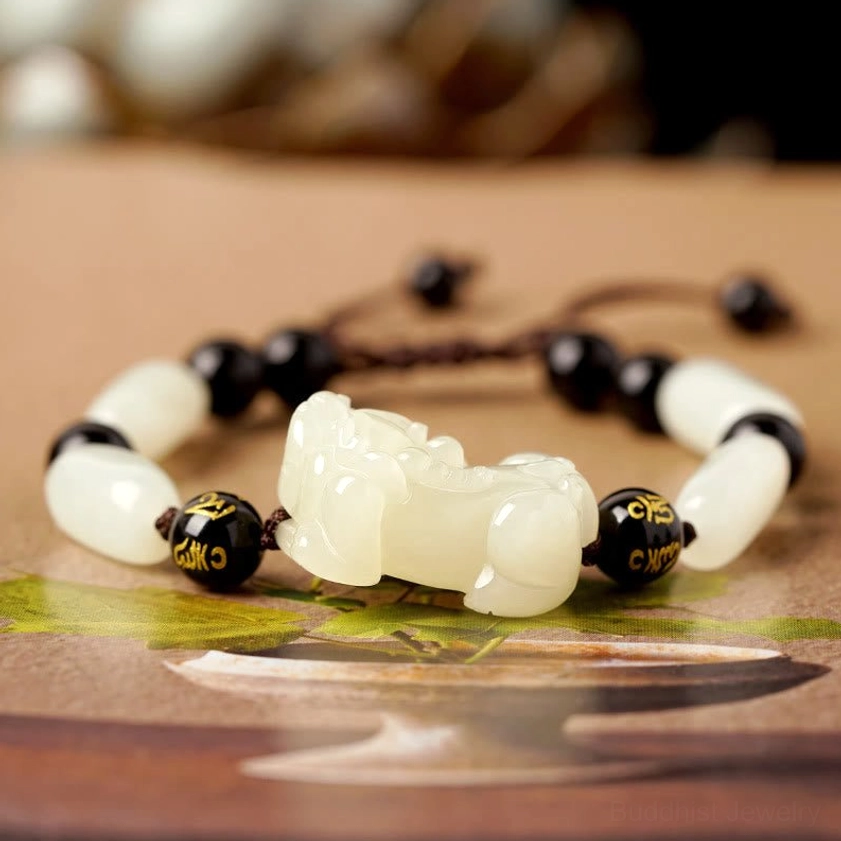 White jade and black engraved bead Pixiu bracelet, oblique angle detail shot with natural backdrop