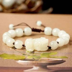 White jade Pixiu bracelet with brown cord, front view on tabletop with natural leaf decorations