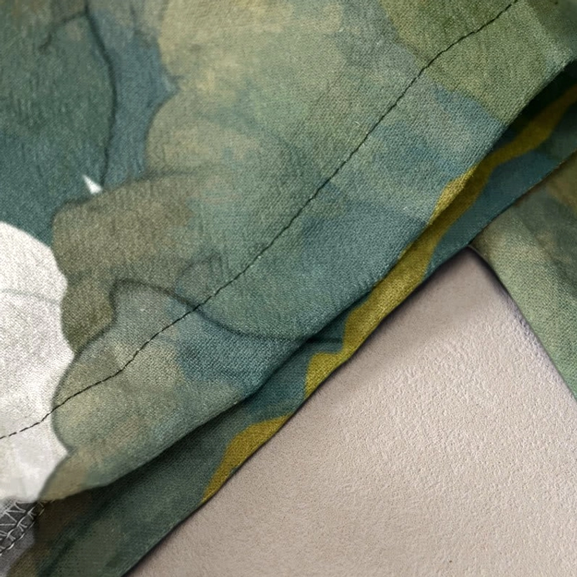 Fabric texture close-up showing white lotus print on green cotton with visible seams and weave