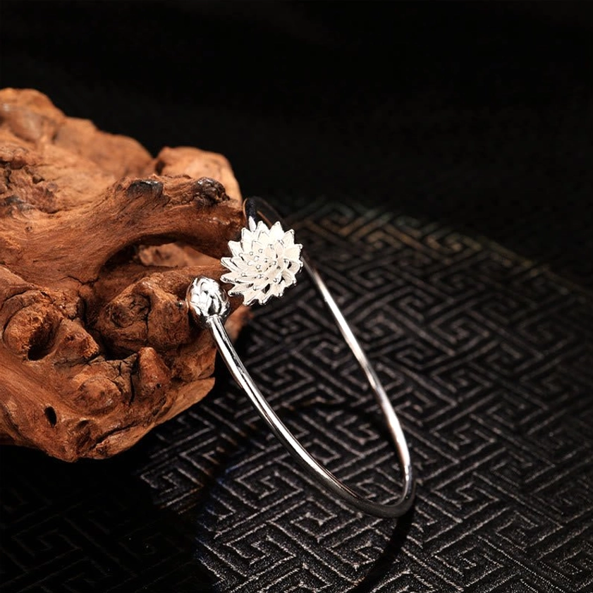 White lotus open cuff bangle with detailed bloom and accent charm, left oblique view on driftwood