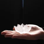 White lotus liuli crystal incense burner held in palm, overhead view, frosted glass with detailed petal carving