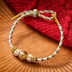 White braided rope Om Mani Padme Hum wisdom bracelet with gold-toned mantra bead and decorative knot, top-down flat lay view