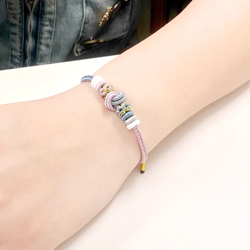 Light blue and purple lucky string bracelet worn on wrist with denim background showing braided knot detail