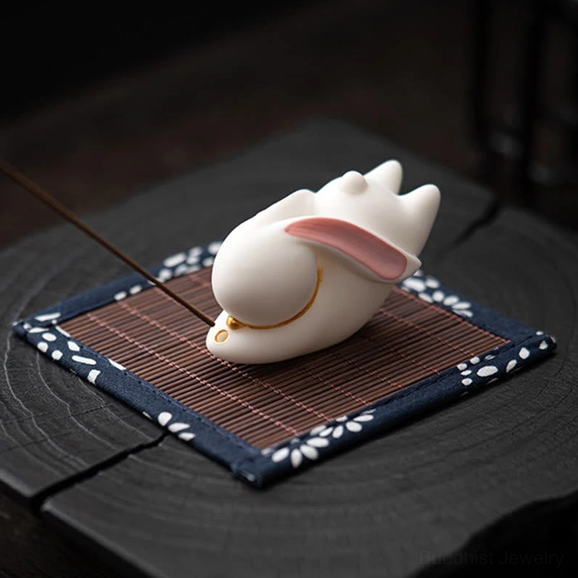 White ceramic rabbit incense holder with gold decorative trim on blue floral cloth mat side angle