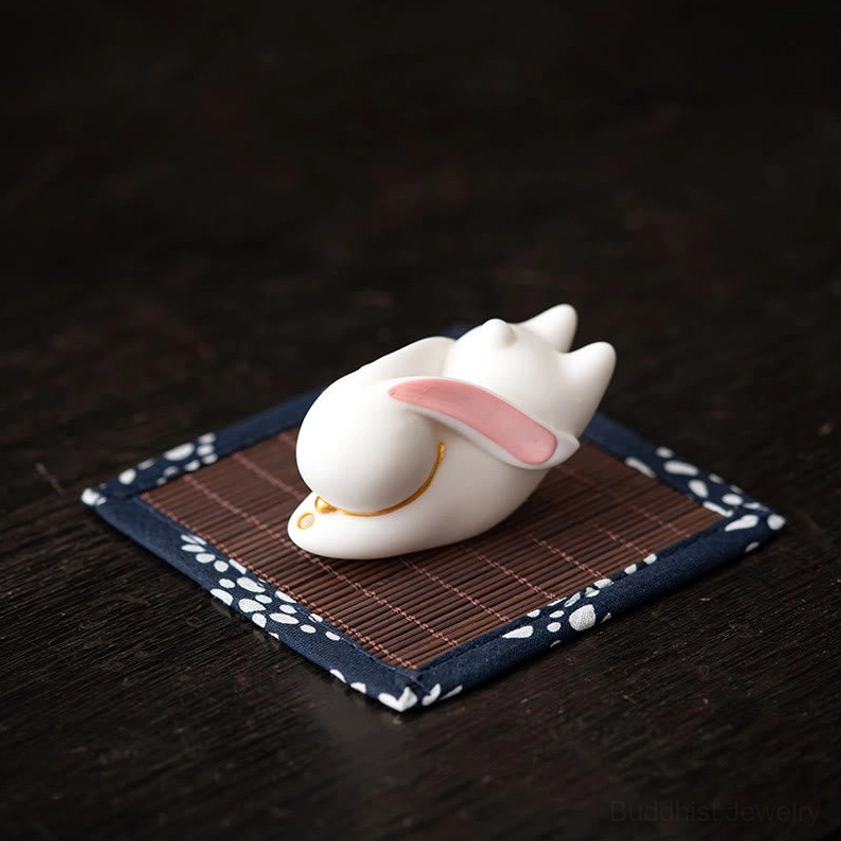 White ceramic rabbit decorative piece with smooth glazed finish on blue floral bamboo mat top-down view