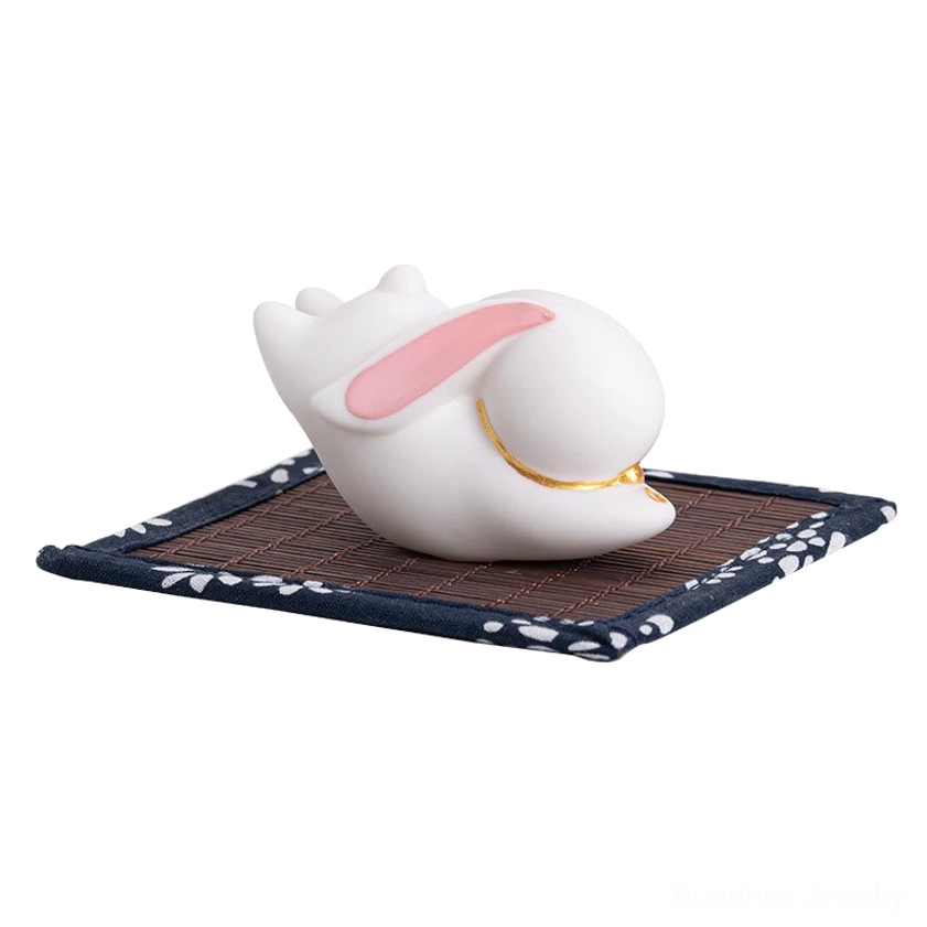 White ceramic rabbit incense holder with pink inner ears and gold accents on blue floral bamboo mat front view