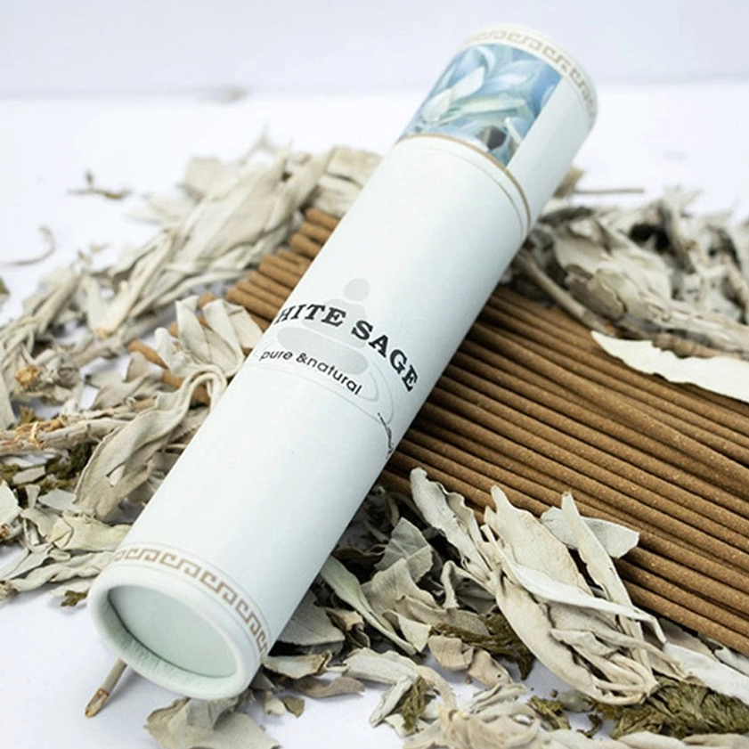 Stacked white sage incense sticks with paper tube on dried sage leaf background overhead view