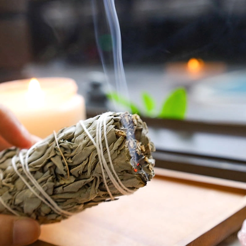 Lit white sage smudge stick burning with visible smoke and charred end for energy purification and meditation