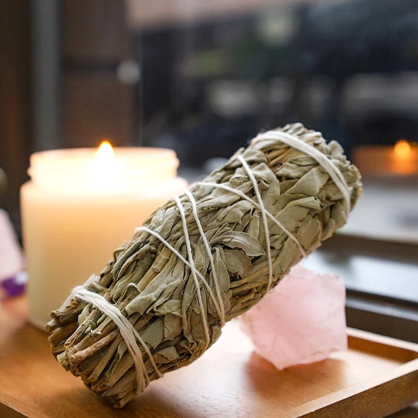 White sage smudge stick placed on wooden tray with candle and rose quartz crystal for energy work