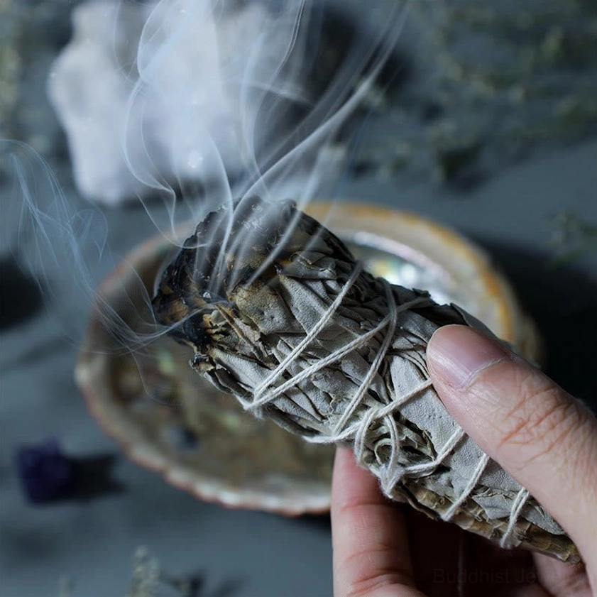 Hand holding burning white sage smudge stick with visible smoke for spiritual cleansing ritual