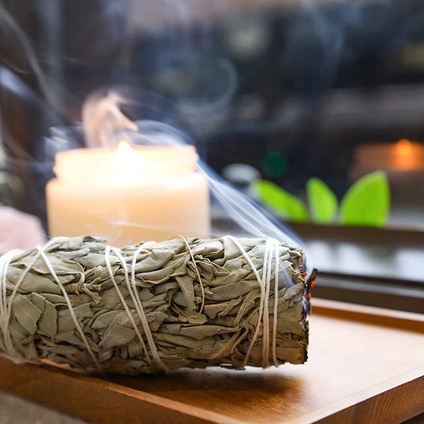 Single white sage smudge stick lit with rising smoke and natural cotton twine binding for spiritual cleansing