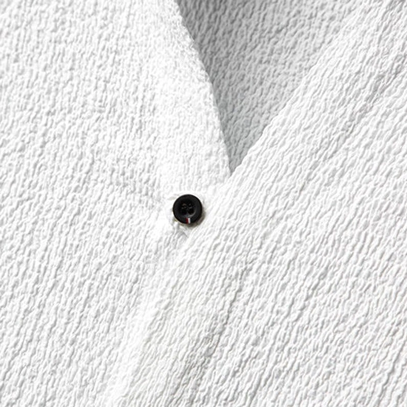 Close-up detail of white textured stand collar shirt showing single black button and wrinkled fabric quality
