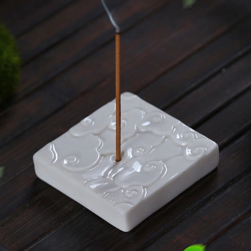 White ceramic square cloud incense burner on wooden surface, high-angle close-up showing embossed cloud texture, matte white glaze, and lit incense with visible smoke