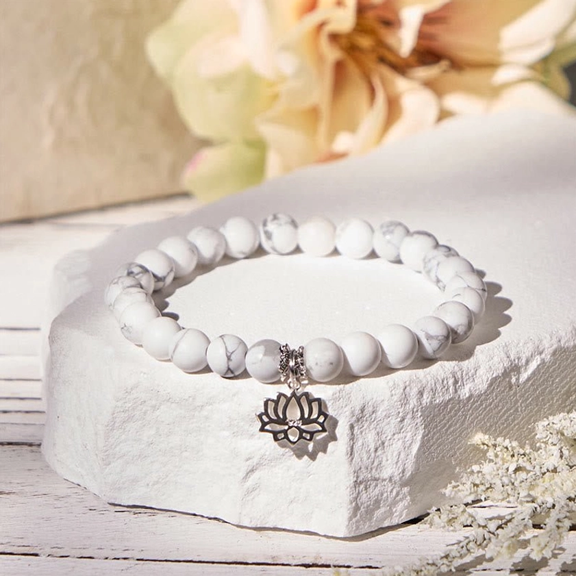 Handmade white turquoise lotus bracelet displayed on curved stone surface with floral styling and silver lotus pendant detail