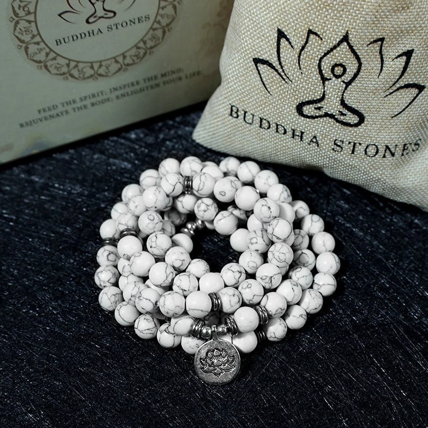 Piled white turquoise lotus mala beads display with silver metal accents and lotus charm on black flannel with branded cushion