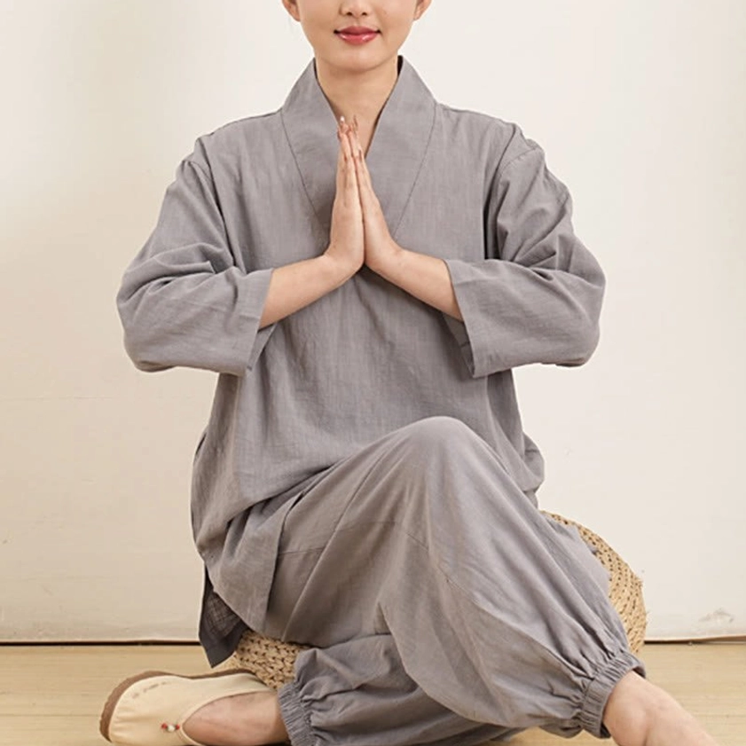 Women in gray meditation clothing kneeling in prayer position indoors, spiritual practice