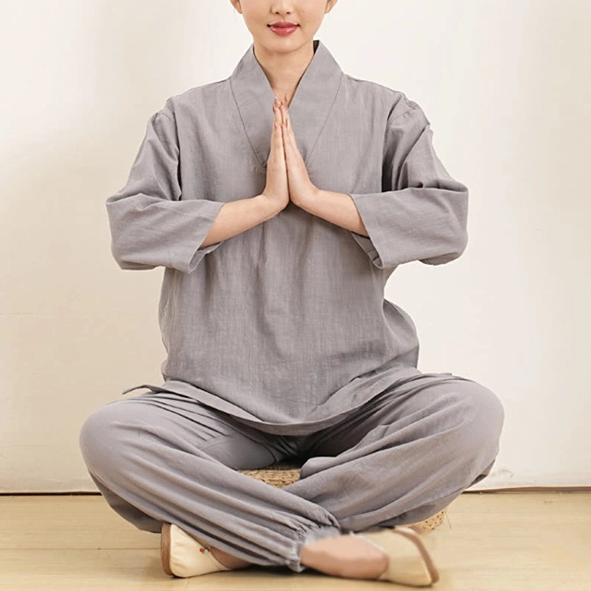 Woman wearing gray three-quarter sleeve meditation clothing in front prayer pose seated
