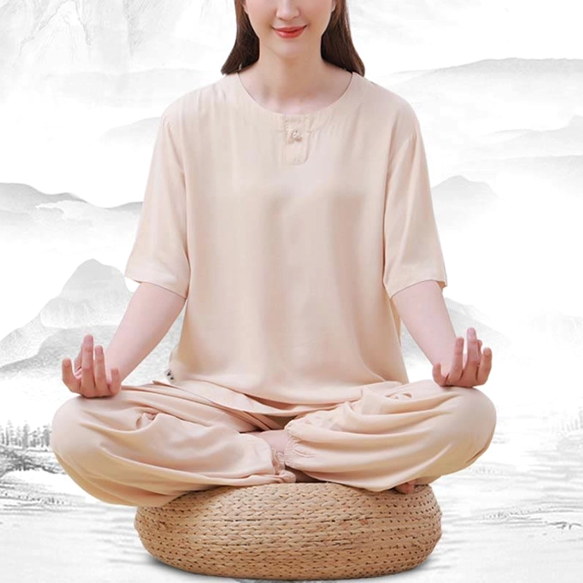 Front view of beige meditation clothing set on model sitting cross-legged on cushion, showing loose fit crew neck top and comfortable pants