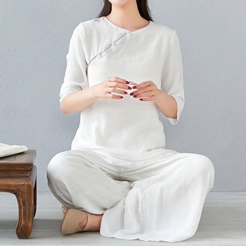Woman seated cross-legged in white long-sleeve meditation cotton linen set with full-length wide-leg pants, simple indoor studio setting