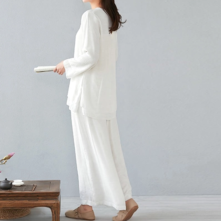 Side profile of woman wearing white long-sleeve meditation linen set with floor-length wide-leg pants holding book, Chinese tea room setting