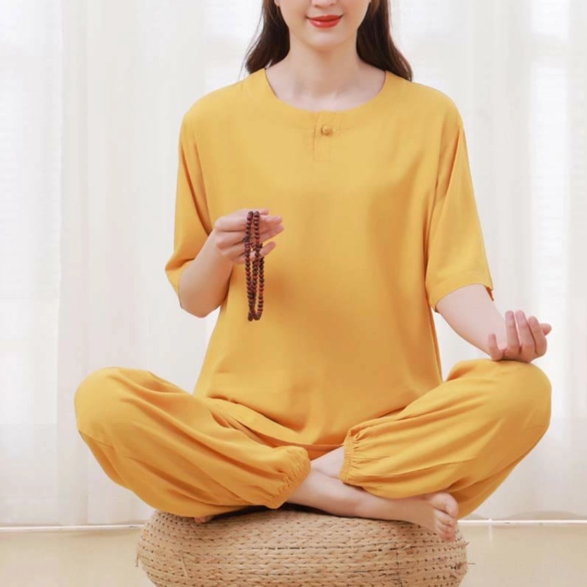 Front seated view of yellow meditation wear set on cushion showing solid yellow crew neck top and loose elastic waist pants with prayer beads