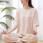 Women's beige zen meditation tai chi cotton clothing set, three-quarter side view of seated woman wearing crew neck half sleeve top with frog buttons and elastic waist pants