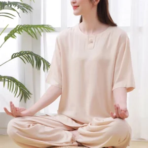 Women's beige zen meditation tai chi cotton clothing set, three-quarter side view of seated woman wearing crew neck half sleeve top with frog buttons and elastic waist pants