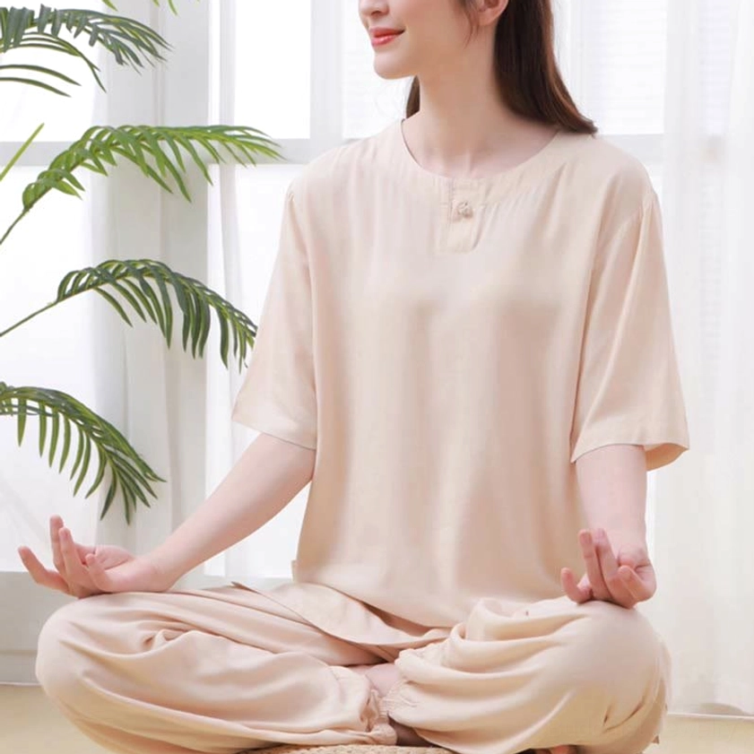 Women's beige zen meditation tai chi cotton clothing set, three-quarter side view of seated woman wearing crew neck half sleeve top with frog buttons and elastic waist pants