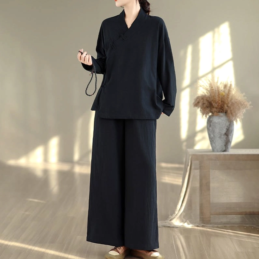 Full body front pose of woman in all-black zen meditation yoga uniform showing v-neck cross collar and frog buttons