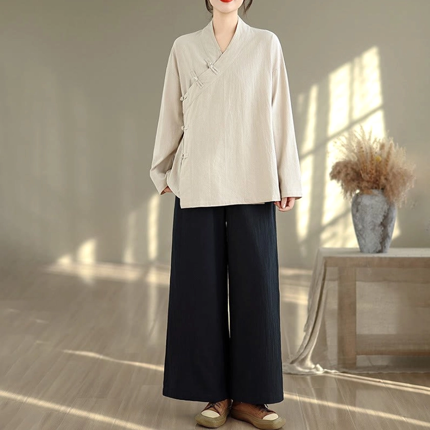 Full body front pose of women wearing beige zen meditation yoga uniform with v-neck cross collar and black wide-leg pants