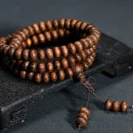 108 wood bead mala necklace with textured natural beads and knotted tassel pendant, displayed on dark vintage wooden surface
