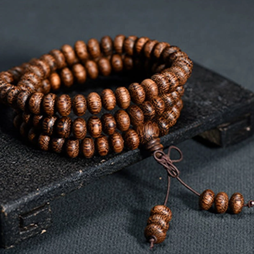 108 wood bead mala necklace with textured natural beads and knotted tassel pendant, displayed on dark vintage wooden surface