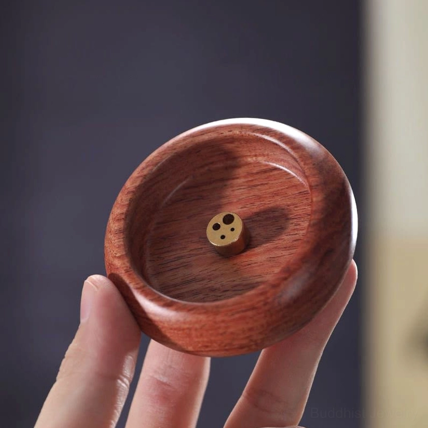 Close-up held view of reddish wood incense holder with natural grain and brass multi-hole insert