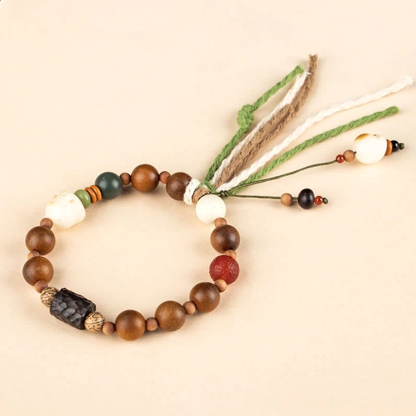 Minimalist top-down flat lay of handmade wooden bracelet with dark wood spacer beads and delicate tassel on beige background