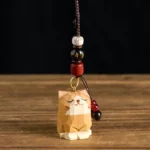 Hand-carved wooden cat Om Mani Padme Hum keychain flat lay overhead view showing faceted carving detail and beaded lanyard