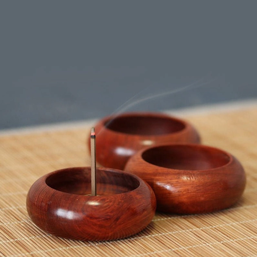 Close-up side view of wooden incense holder with single aromatic stick, showing warm reddish-brown natural wood finish