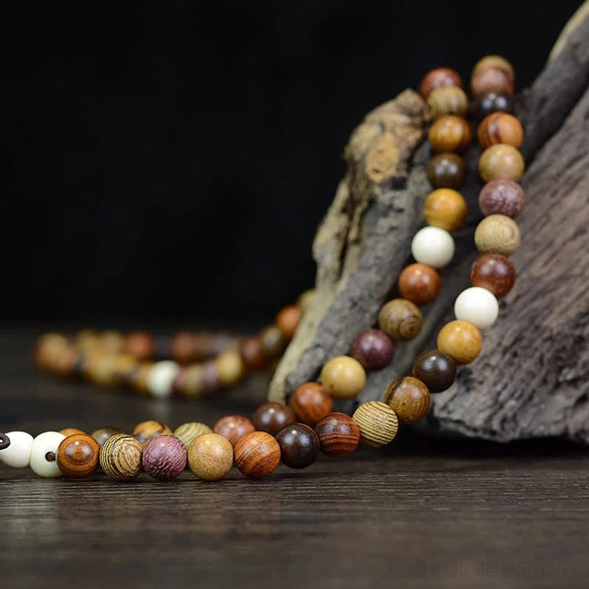Natural wood mala prayer beads draped on dark wooden table with white accent beads and mixed warm wood tones, low-angle side view