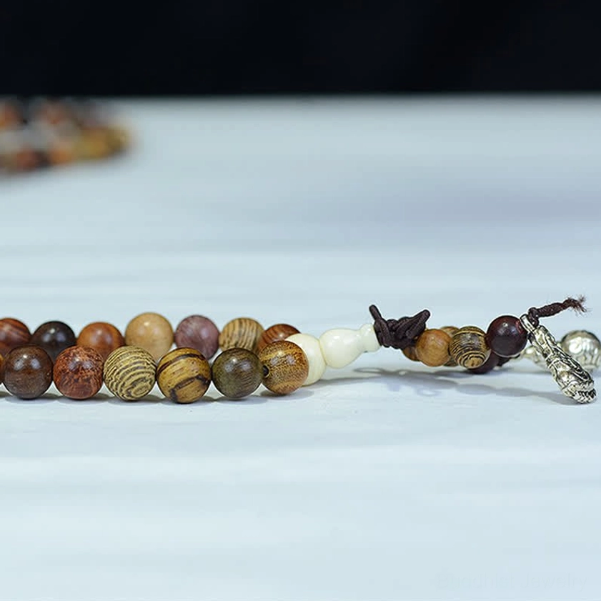 Single strand natural wood mala beads with silver pendant and varied wood grain textures on light blue background, flat lay