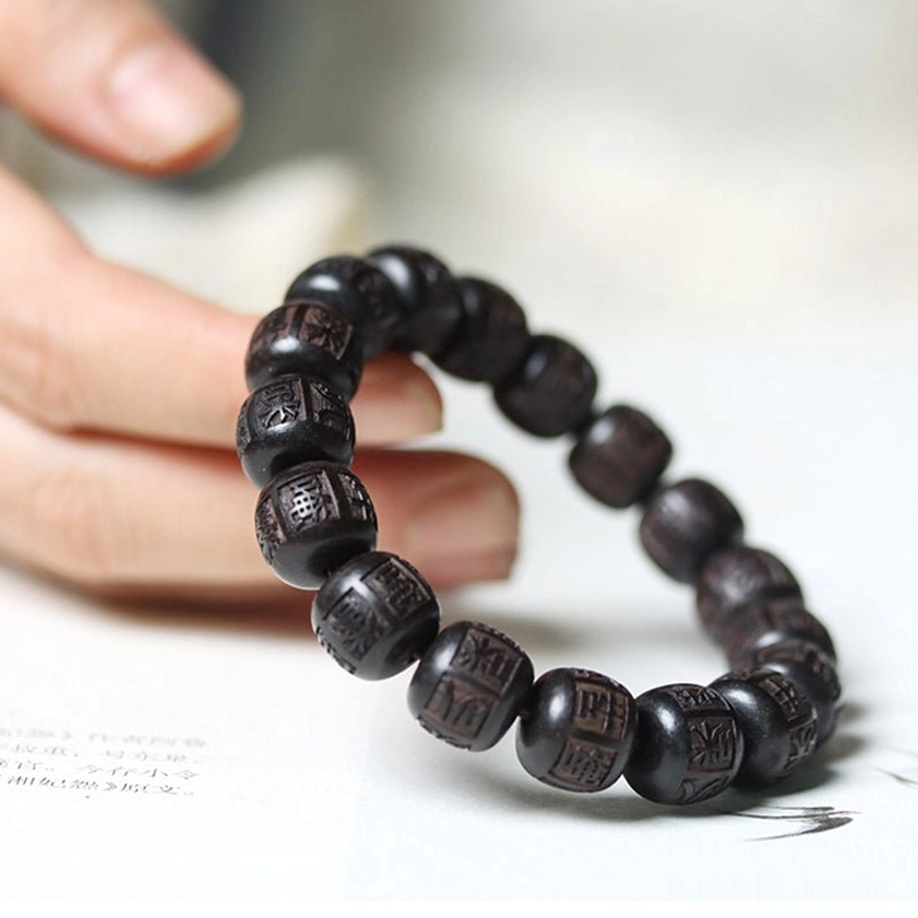 Person holding ebony wood Buddhist bracelet showing clear engraved mantra text on cylindrical beads