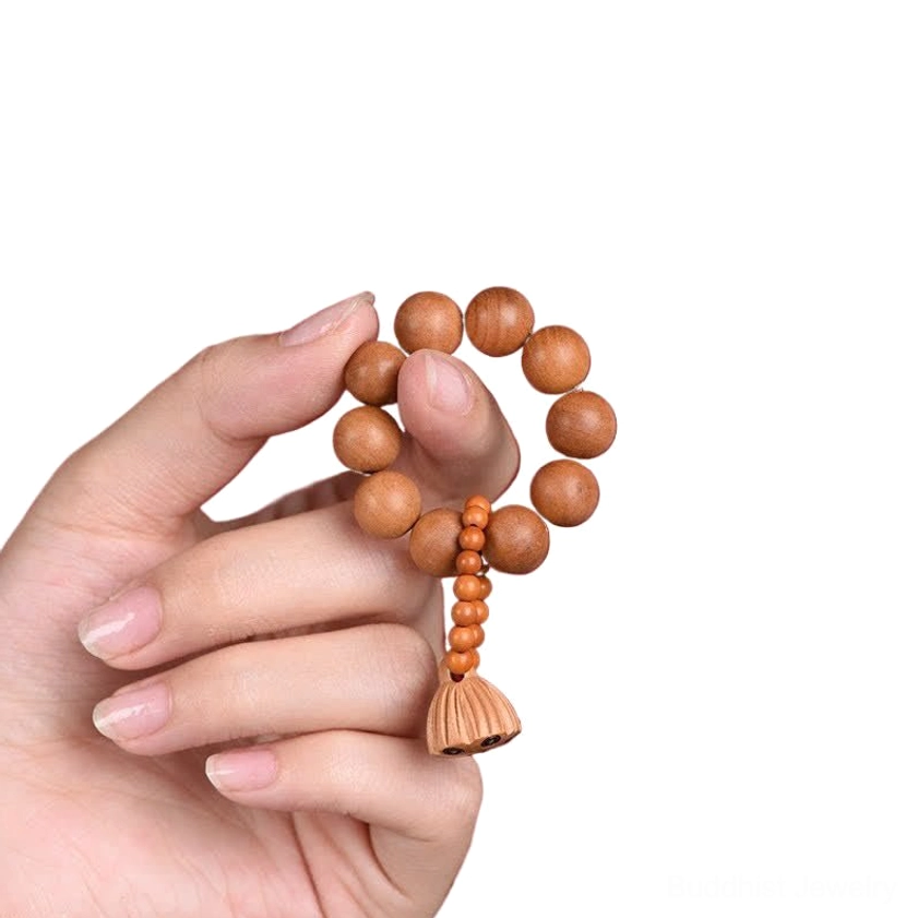 Fingers holding smooth round peach wood meditation prayer beads with lotus pod pendant on light neutral background